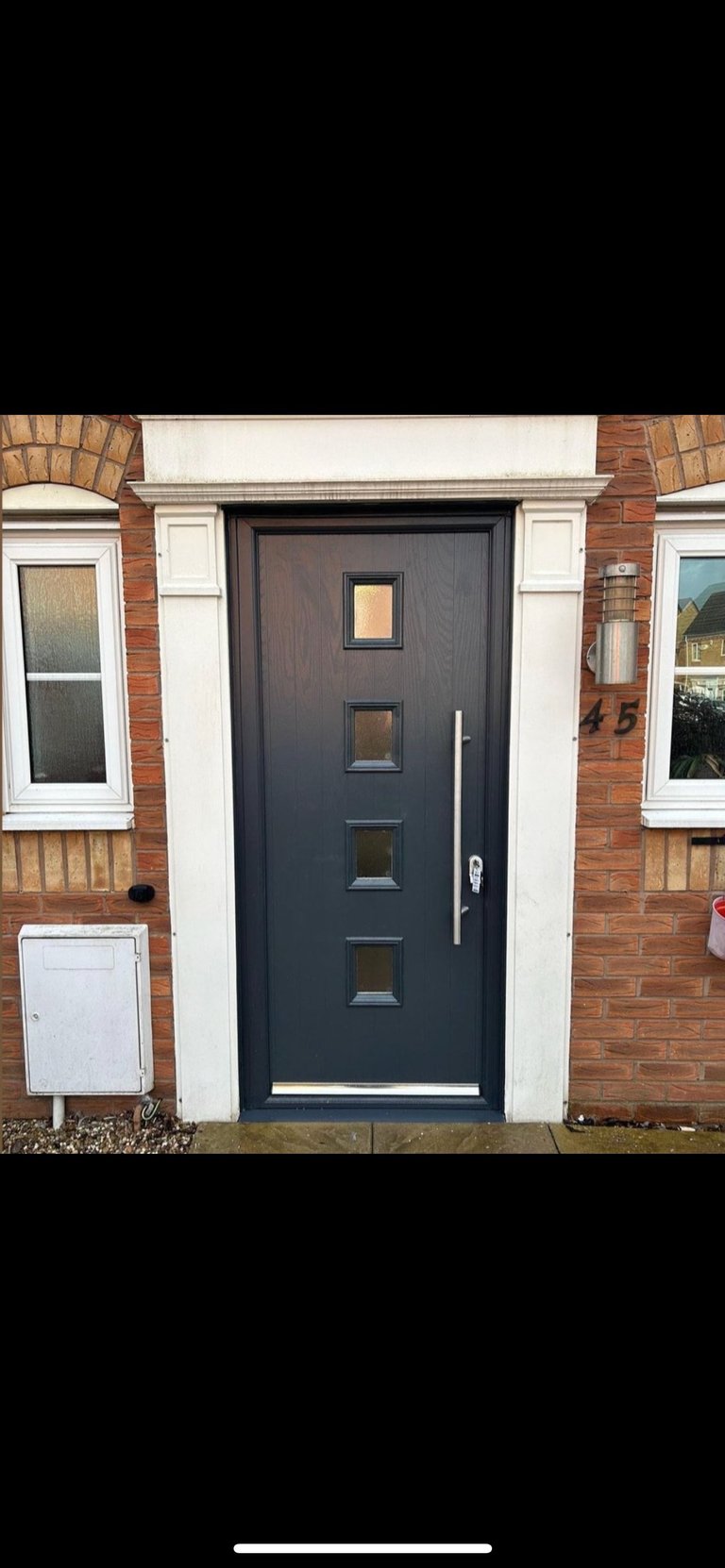 Modern black front door with four glass panels on a brick house facade, flanked by white trim and windows