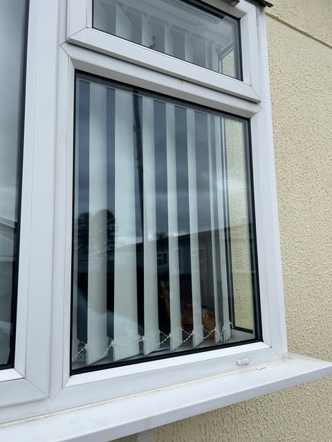 Modern white-framed window with vertical blinds and transom window above, mounted on beige textured wall