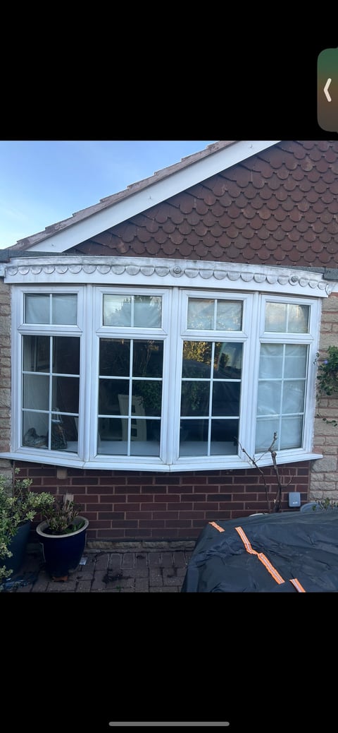 White uPVC bay window with multi-pane glass on brick house with brown tiled roof and decorative gutter trim