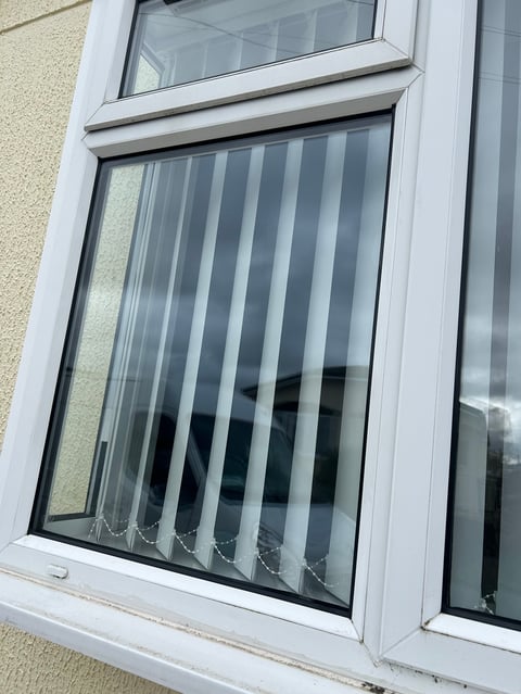 White window frame with vertical blinds closed, exterior wall visible above