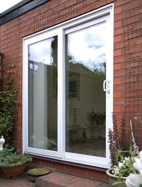 White framed sliding patio doors on a red brick wall with garden plants and flowerpots on the surrounding terrace