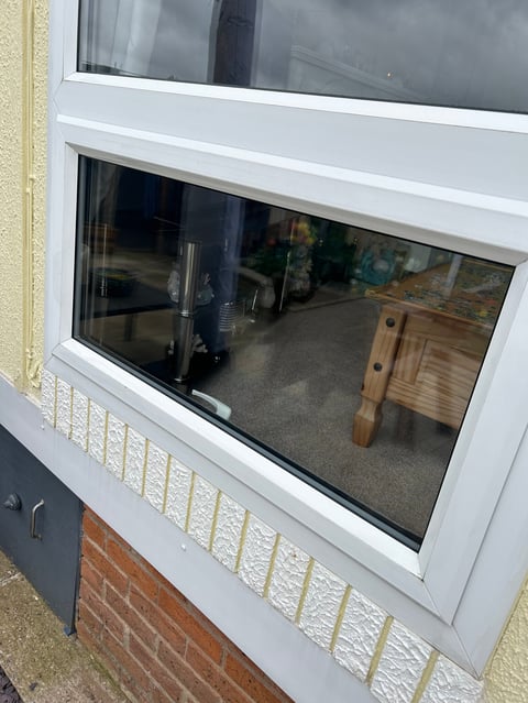 White-framed window with dark tinted glass showing interior garage or workshop space, set above red brick wall with cream-colored trim