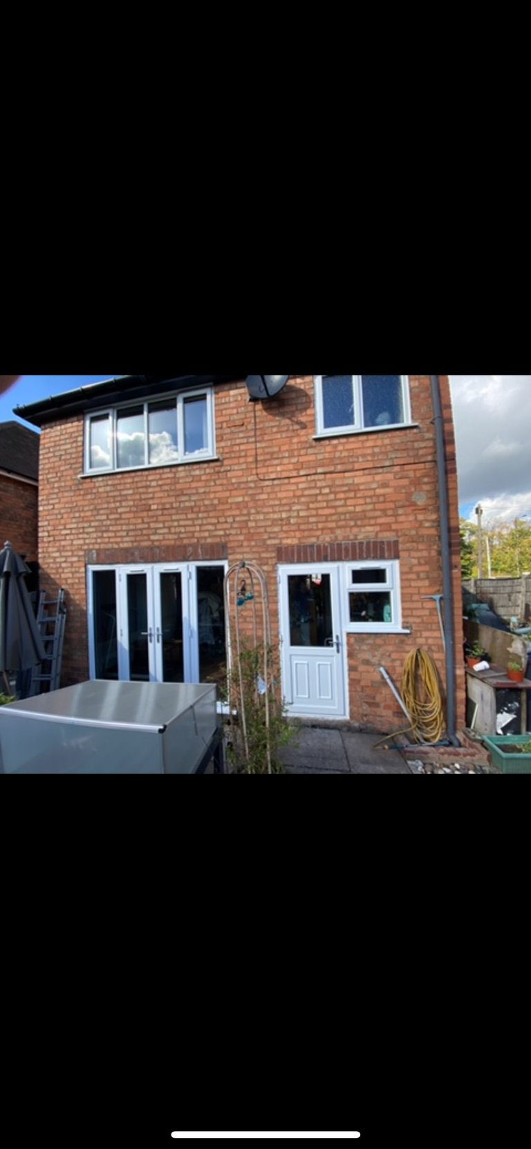 Red brick house with blue-framed bifold doors and white entrance door in patio area with garden equipment