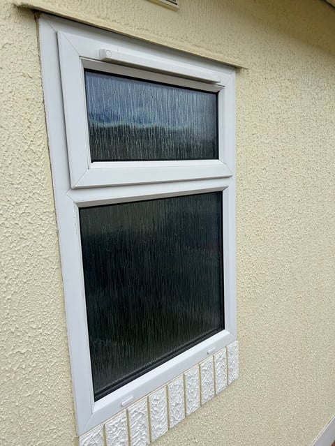 White-framed window with two dark glass panes mounted on a cream textured wall, with a decorative white sill at the bottom