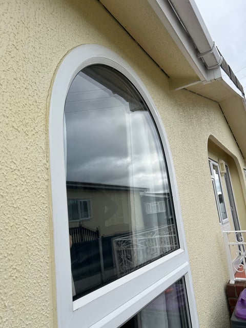 Large arched white-framed window with dark glass on a cream-colored textured wall, with a smaller rectangular window below