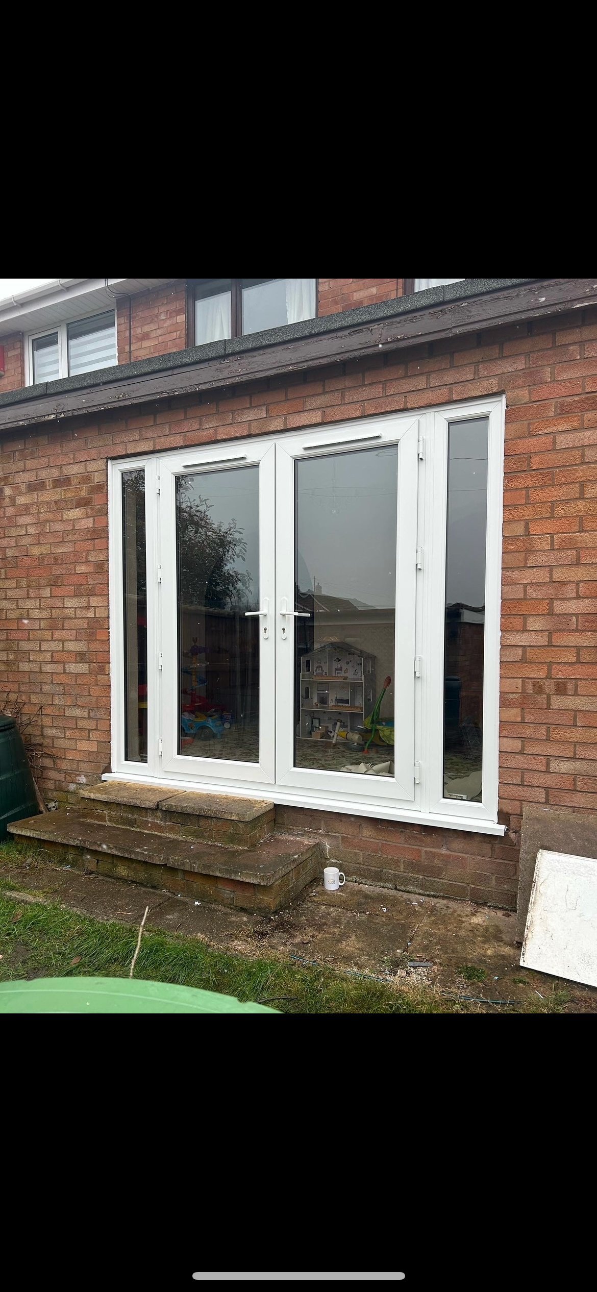 White uPVC patio doors with side panels installed in a brick house exterior, viewed from the garden