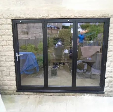 Black triple-pane glass patio doors installed in white brick wall with garden visible through windows